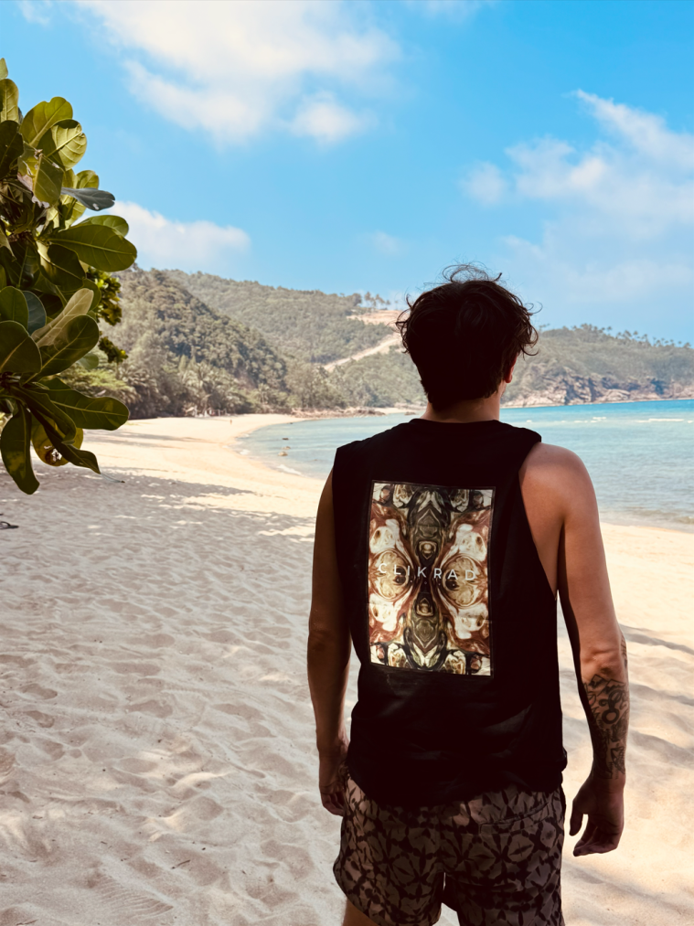Black tank with a key-art back print, worn on a beach.